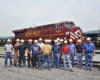 15 men standing in front of red-and-yellow diesel locomotive