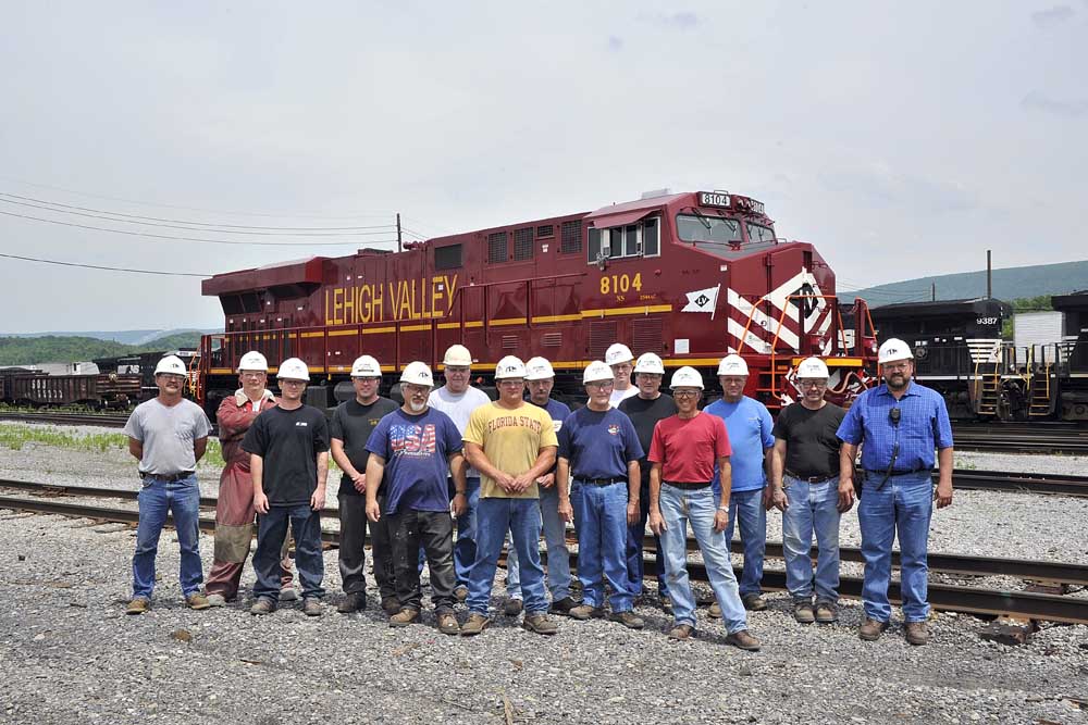 15 men standing in front of red-and-yellow diesel locomotive