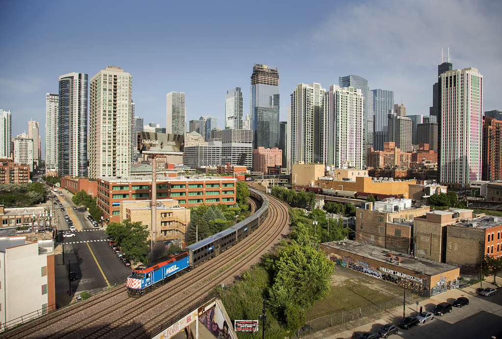Passenger train rounding curve witha city skyline in the background. 