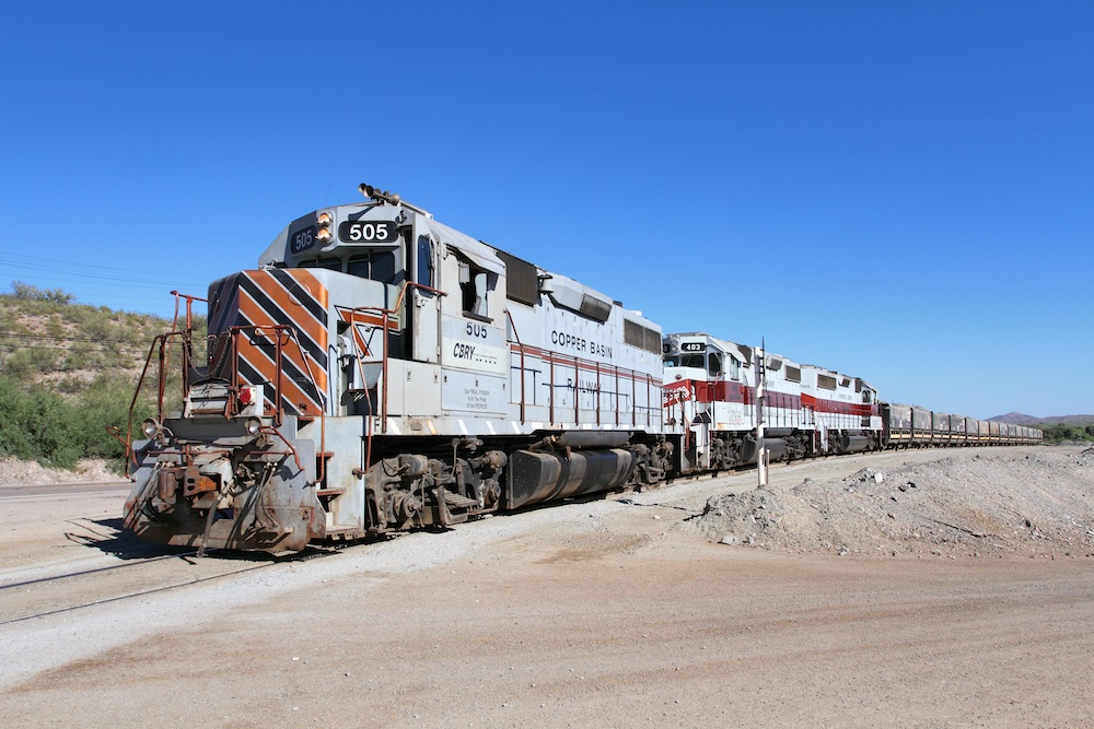 Three grey diesel locomotives pulling ore train.