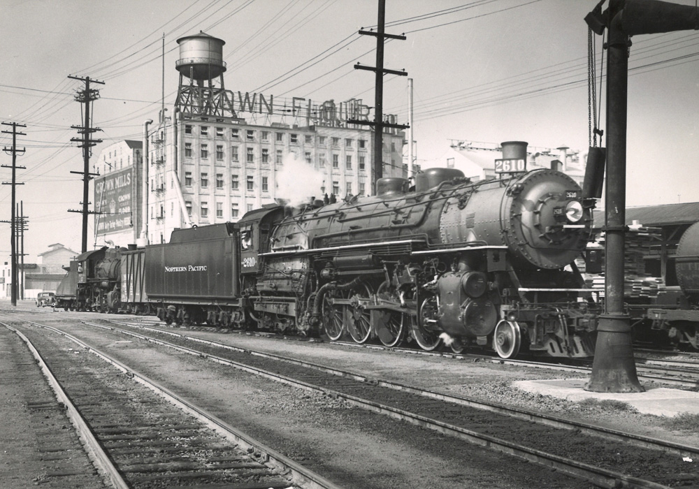 A black-and-white photo of a steam locomotive switching a flour mill