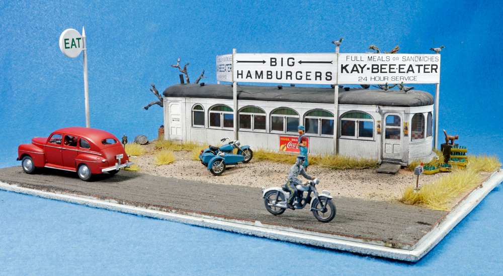 An O scale roadside diner model on a diorama in front of a blue background