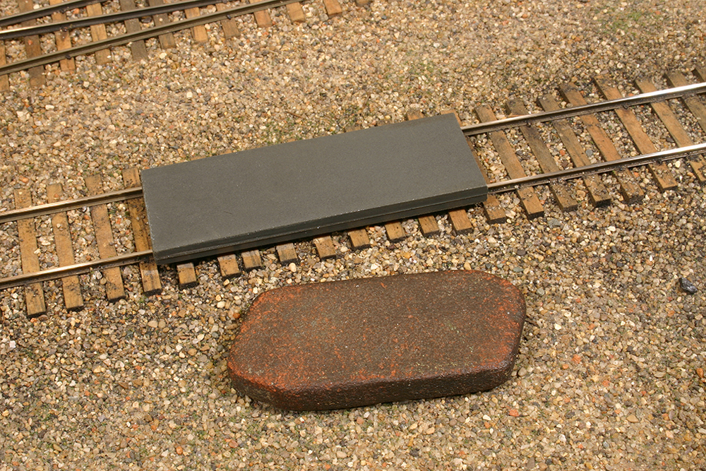 A black rectangular abrasive block and a dark red block near HO scale track