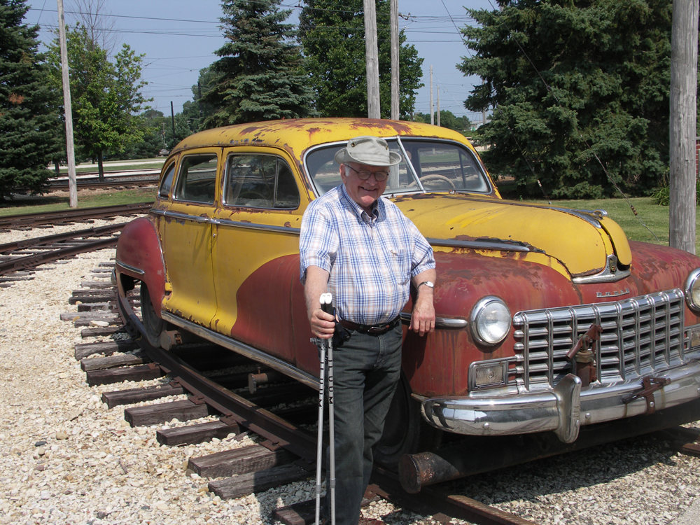 An image of a man standing next to an automobile on railroad tracks.