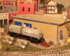 model tank car with gas tanks next to a structure on model train layout
