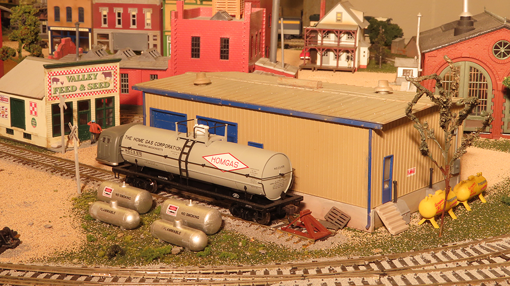 model tank car with gas tanks next to a structure on model train layout