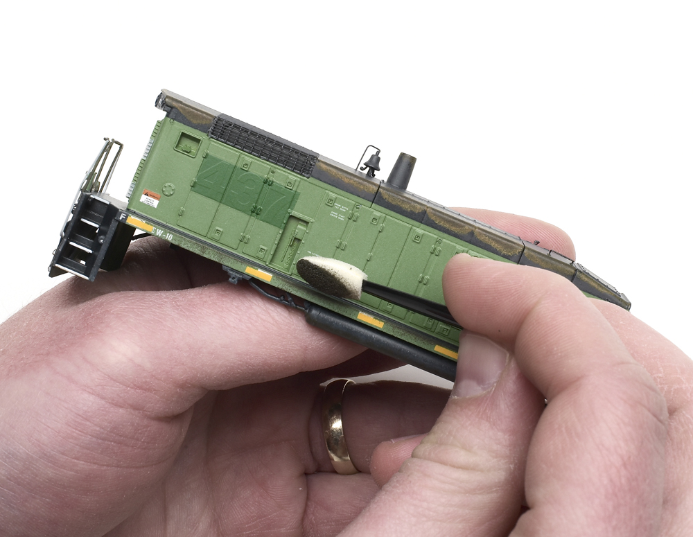 Using cosmetic applicators for weathering: A pair of hands holding a model locomotive with a cosmetic applicator.