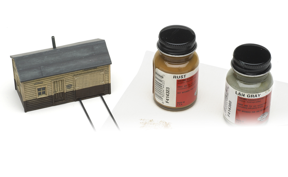 Weathering structures with drybrushing: A structure is shown next to bottles of paint against a white background.