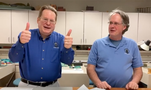 One man with two thumbs up and another looking at him in front of a table.