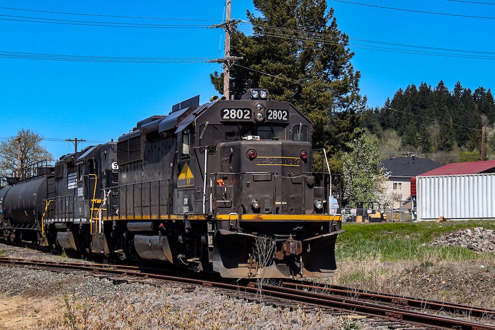 Two brown and black diesel locomotives pulling a freight train of tank cars