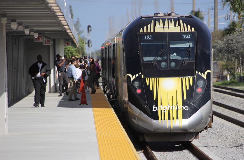 People mill about on platform next to streamlined passenger trains