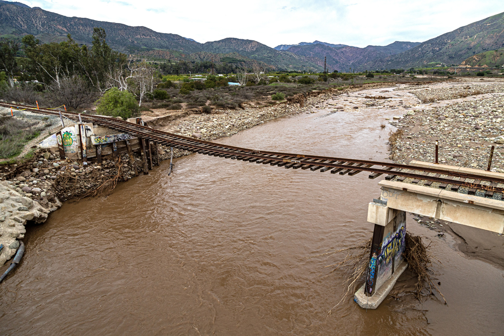 Railroad track hangs over river after bridge has been washed out