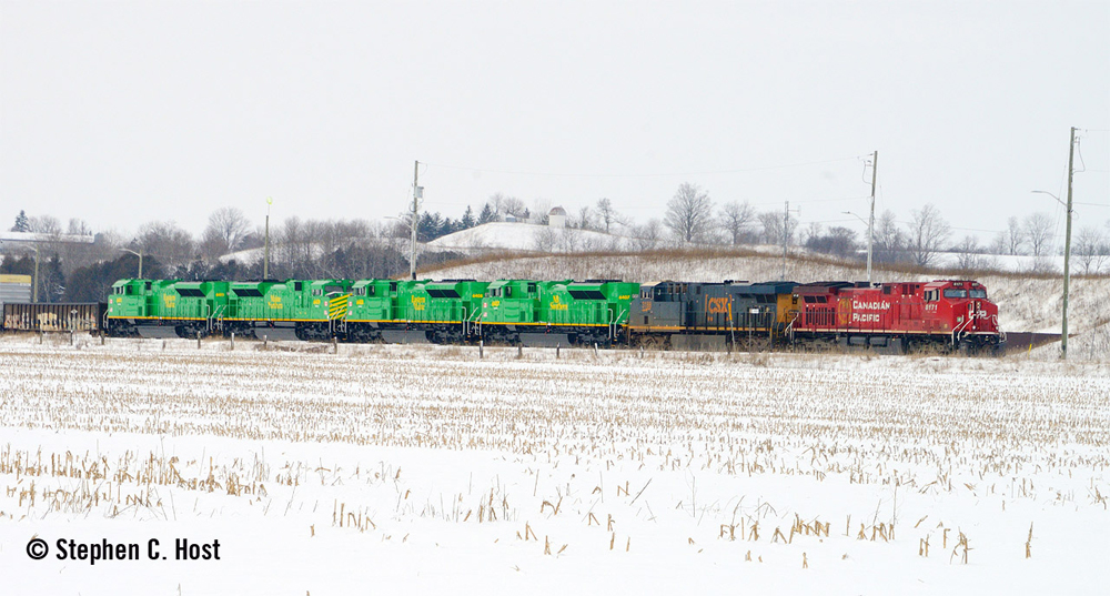 Six locomotives at front of train, including four bright green units being delivered to short lines