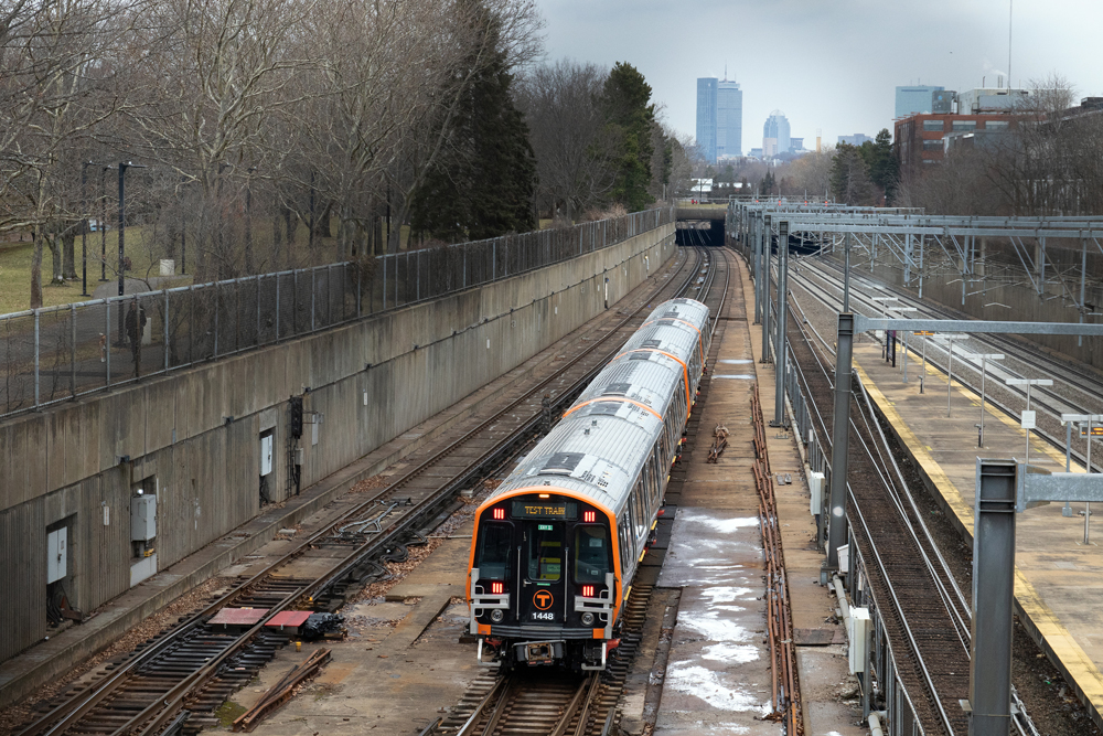 Rapid transit train operates on open-air track with city skyline in distance