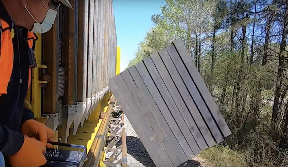 Railroad ties are pushed out of freight car onto ground next to right-of-way