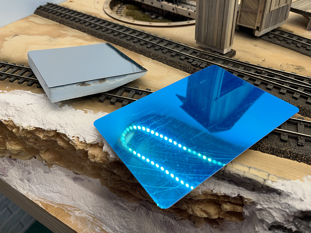 Blue shiny square next to silver square setting on wood table with brown model railroad track on it.