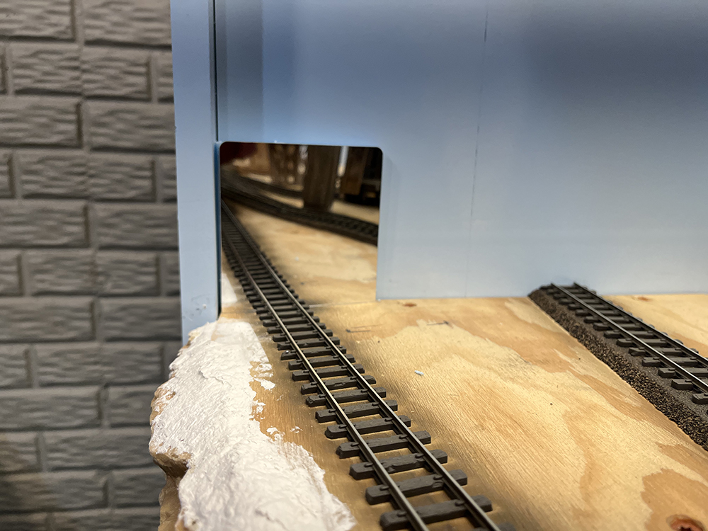 Small mirror attached to blue wall and reflecting brown model railroad track.