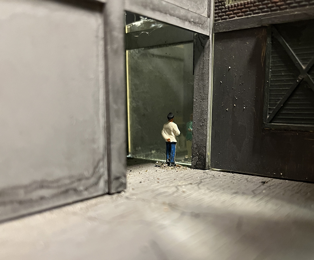Add depth to structures using mirrors: Gray and brown model building walls with open doorway showing two men talking to each other.