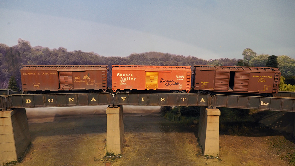 Three brown boxcars on a bridge