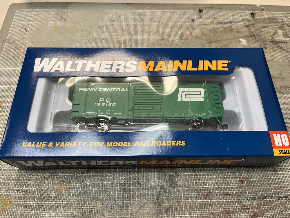 Car Swap Project Part 2: Stripping lettering from models: Green model boxcar in blue and clear package resting on gray workbench