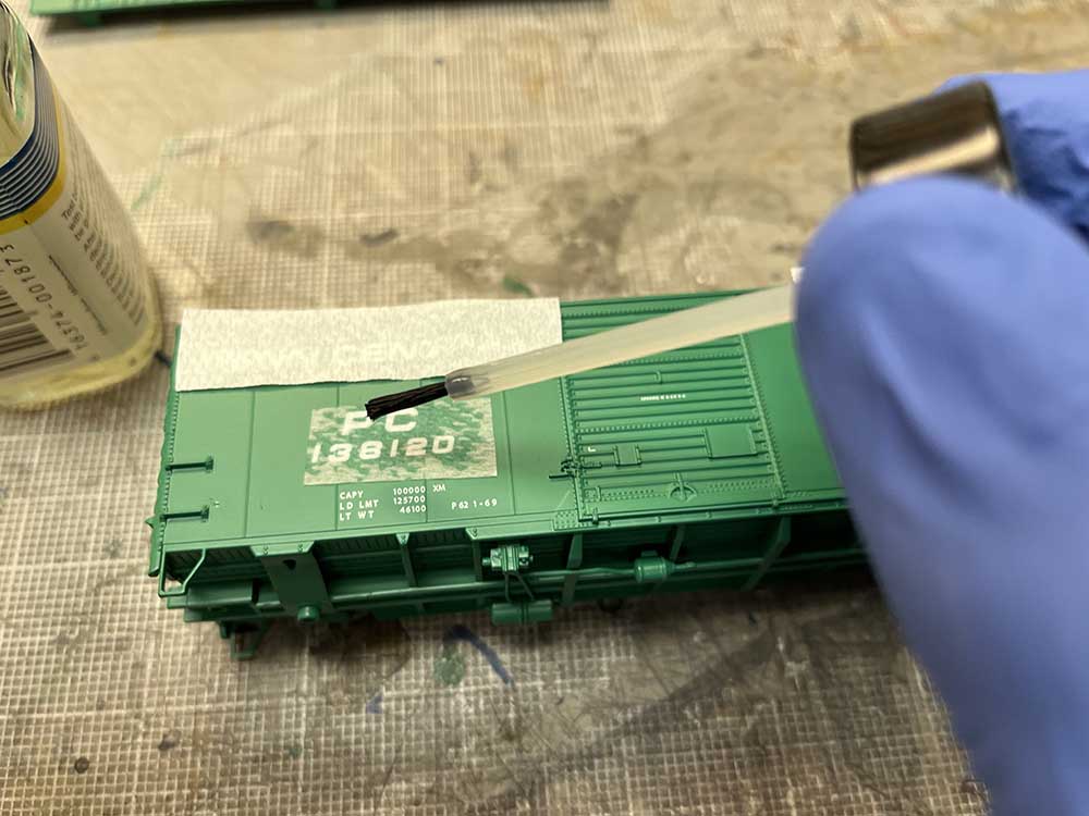 Car Swap Project Part 2: Stripping lettering from models: Hand in blue glove dripping liquid on a paper towel resting on a green model boxcar side