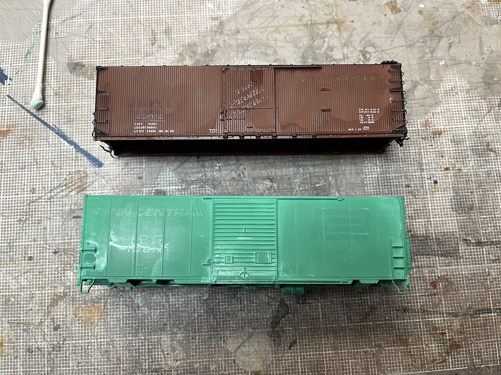 Brown and green model boxcars with faded lettering and paint on gray workbench