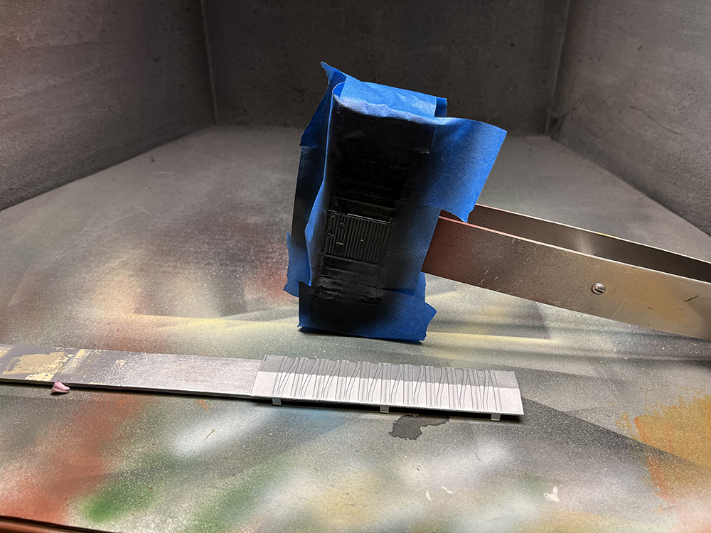 Car Swap Project Part 3: Painting plastic models - Model covered in blue tape and black paint resting on side in grimy spray-painting booth.