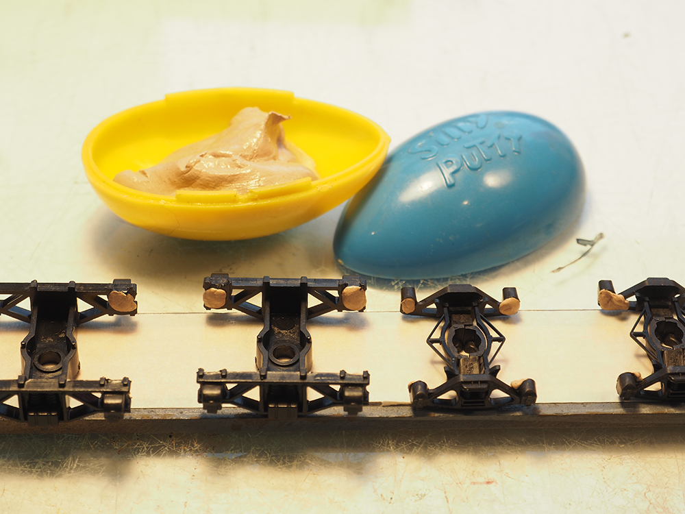 Blue and yellow plastic container with tan putty inside next to black plastic parts