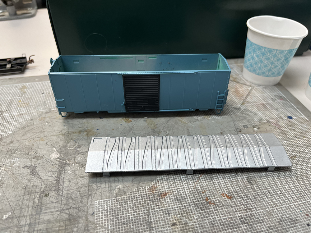 Blue and black plastic boxcar on gray workbench with silver roof removed.