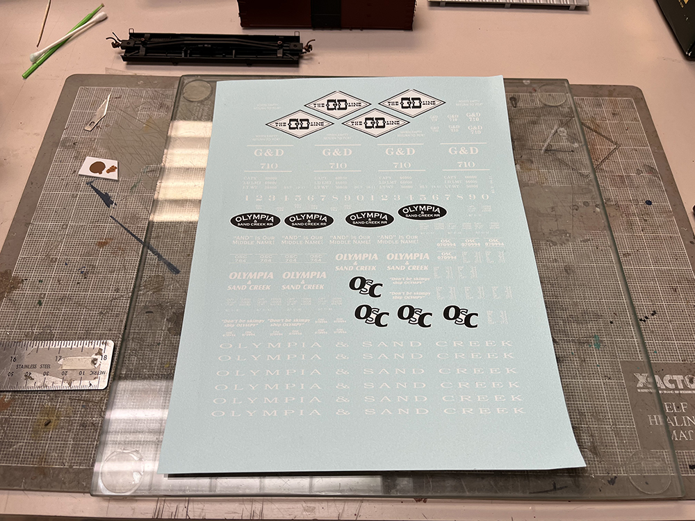 Light blue decal sheet with white and black lettering resting on glass-topped workbench