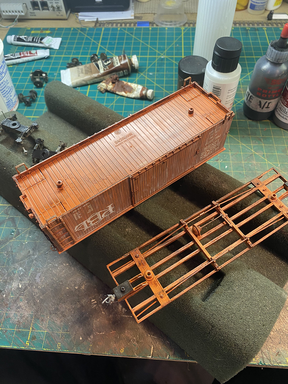 Plastic red boxcar on workbench surrounded by assorted paints and tools.