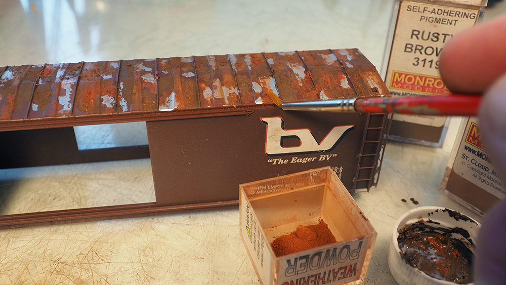 Brown model boxcar with patches of rust-colored powder on roof