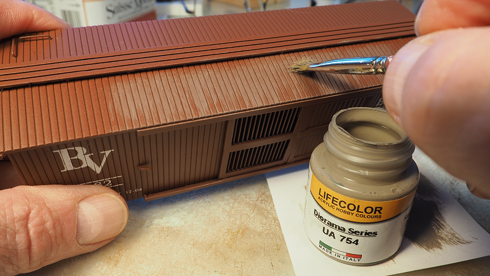 Hands using a small brush to paint tan paint on a brown model boxcar