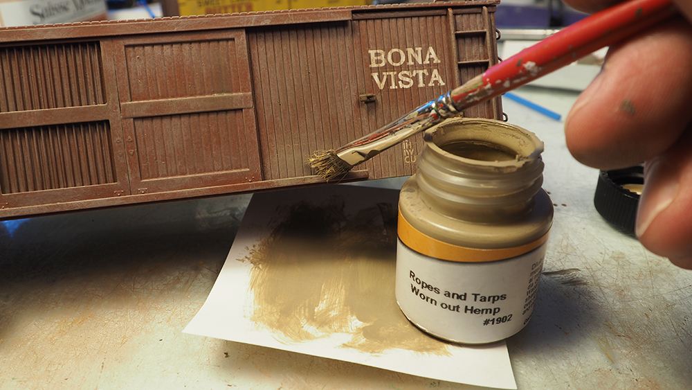 Red paint brush applying tan paint to brown boxcar model