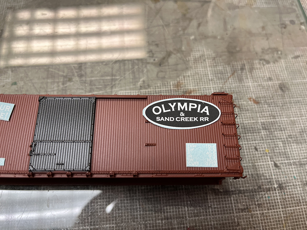 Car Swap part 8 – Olympia cars and liquid rust techniques: Small black and white decals on plain brown boxcar