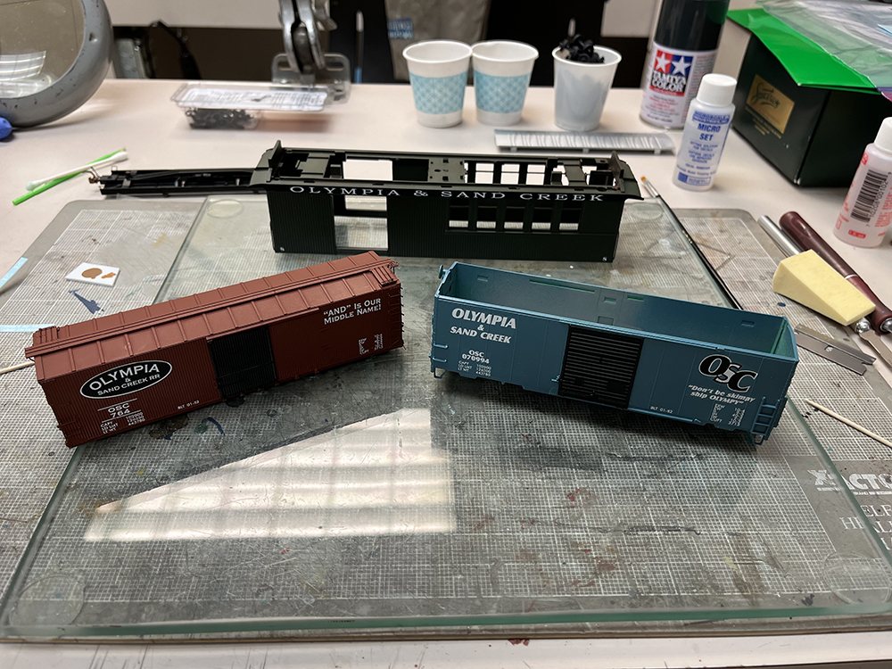 Car Swap part 8 – Olympia cars and liquid rust techniques: Blue, brown, and green model railroad cars on glass workbench