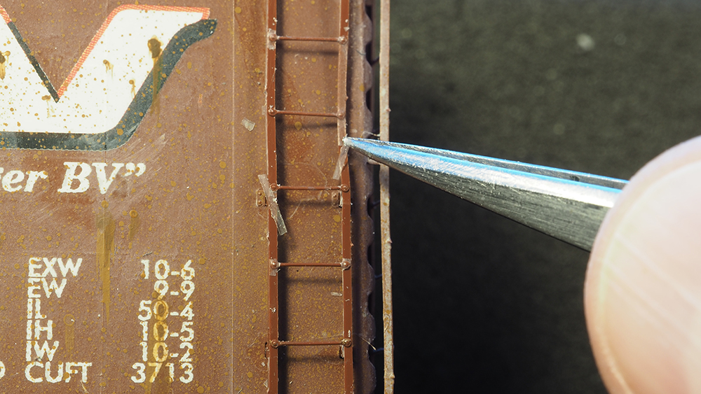 brown plastic ladder held by silver tweezers with flaking white paint.