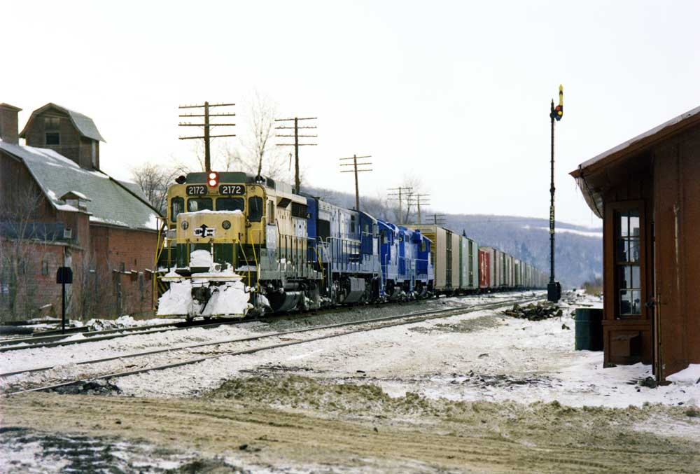 Green-and-yellow locomotive leads three blue locomotives in a classic Conrail scene with snow