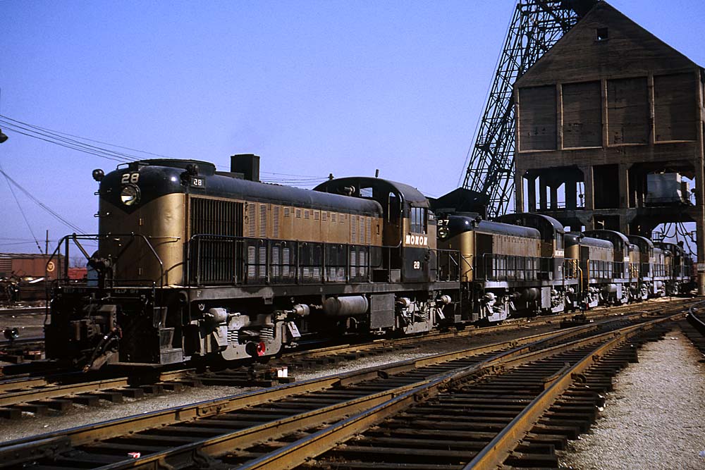 Black-and-gold Monon Railroad diesel locomotives under concrete coaling tower