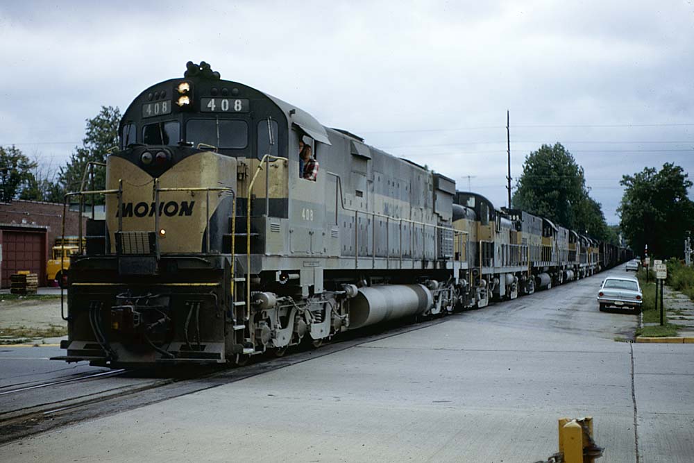 Black-and-gold Monon Railroad diesel locomotives with freight train on street trackage