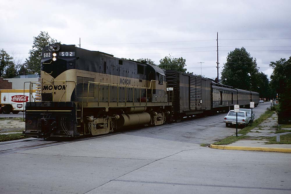 Black-and-gold Monon Railroad diesel locomotive with passenger train on street trackage