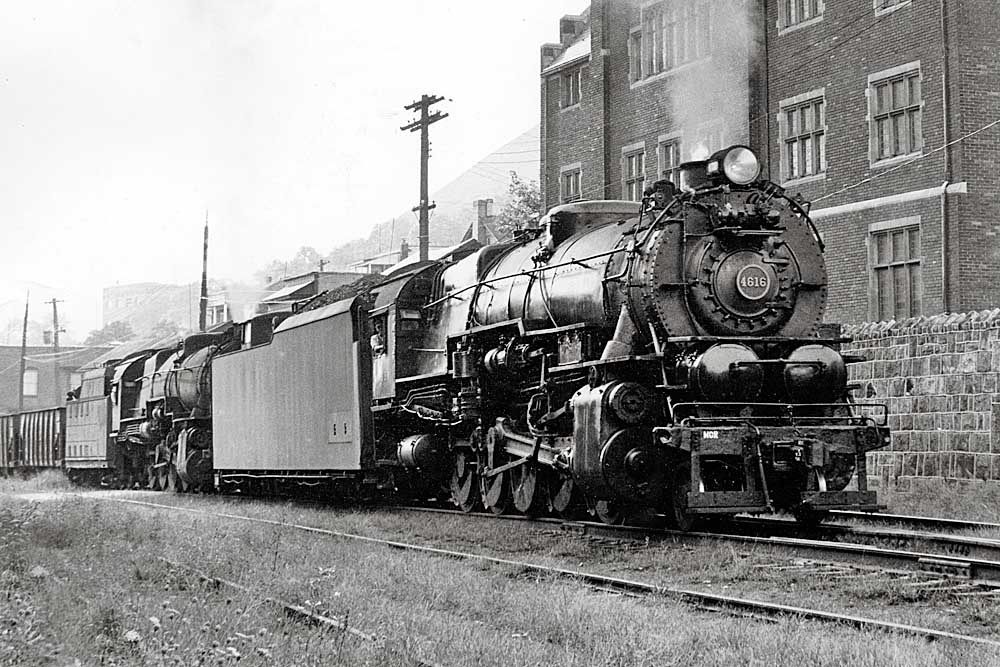 Two steam locomotives lead a train through a city
