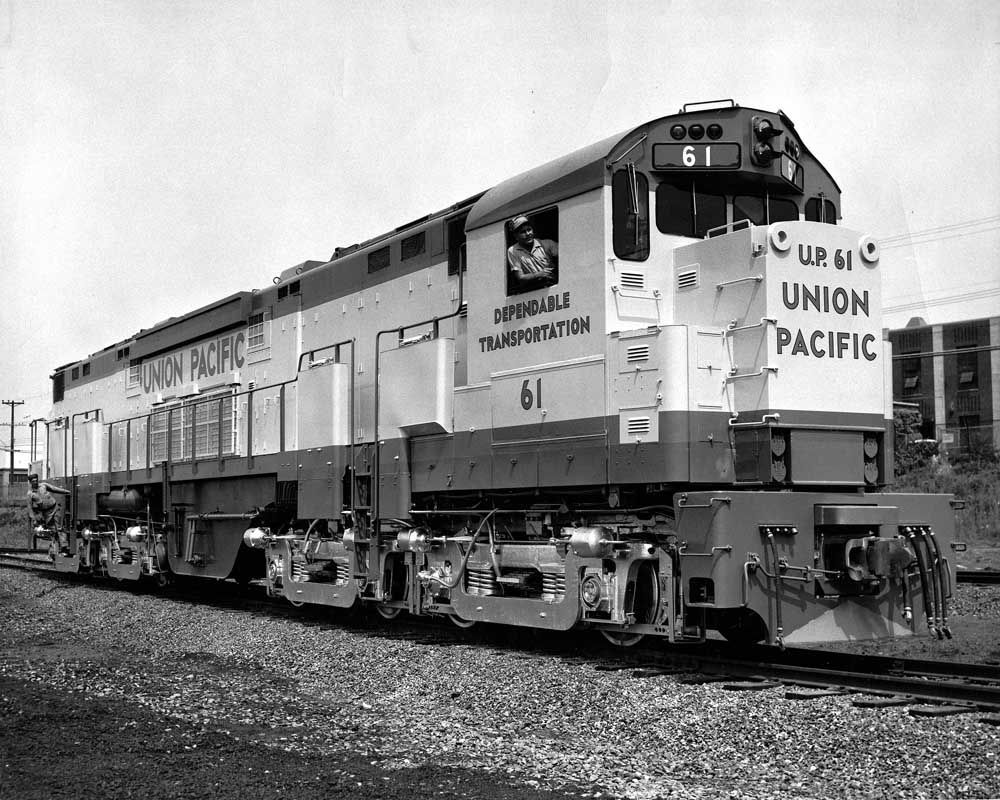Alco C855 locomotives in a freight yard with man in cab window