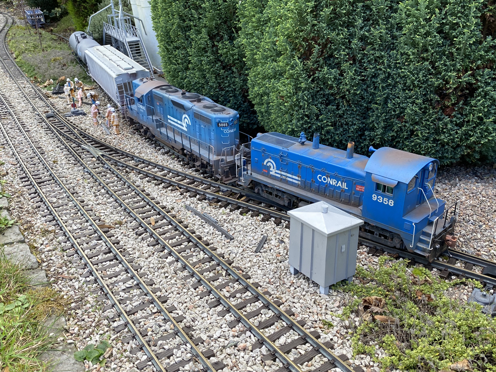 two blue model locomotives rounding a curve on a garden railroad