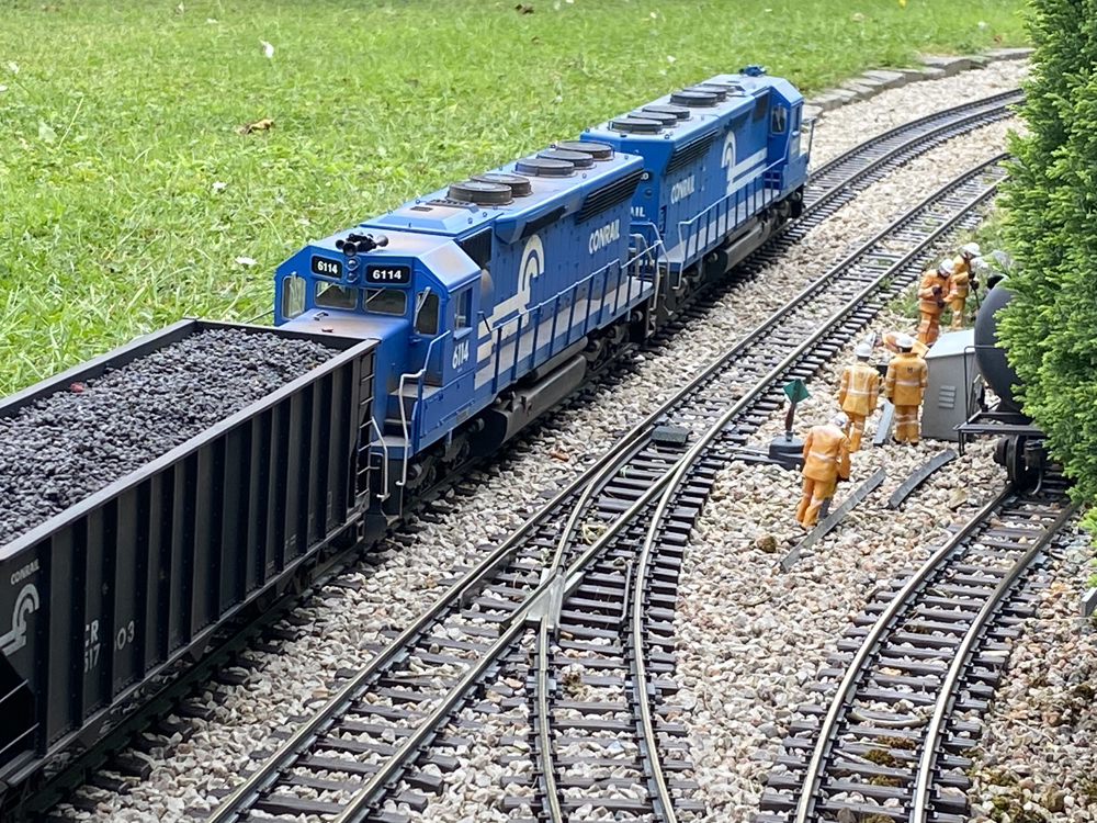 two blue model engines nearing a curve with model people to the right