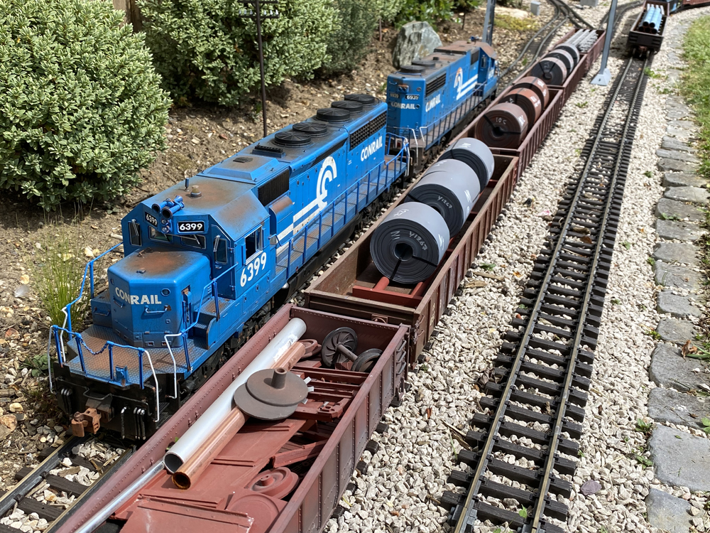 two blue model trains with cars on a garden railroad