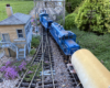 A train approaches a switch tower on a garden railroad