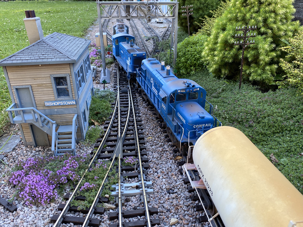 A train approaches a switch tower on a garden railroad
