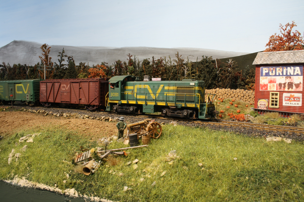 A green switcher pulls a mixed freight trough the countryside