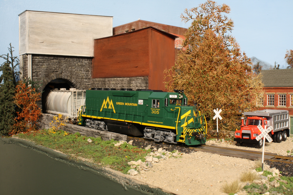 A green diesel locomotive pulls a train through a model tunnel